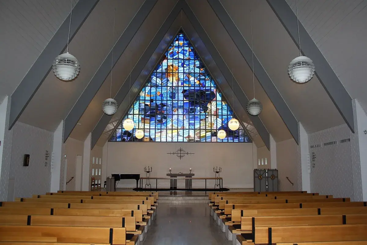 Interior of a modern church with wooden pews and a large stained-glass window.