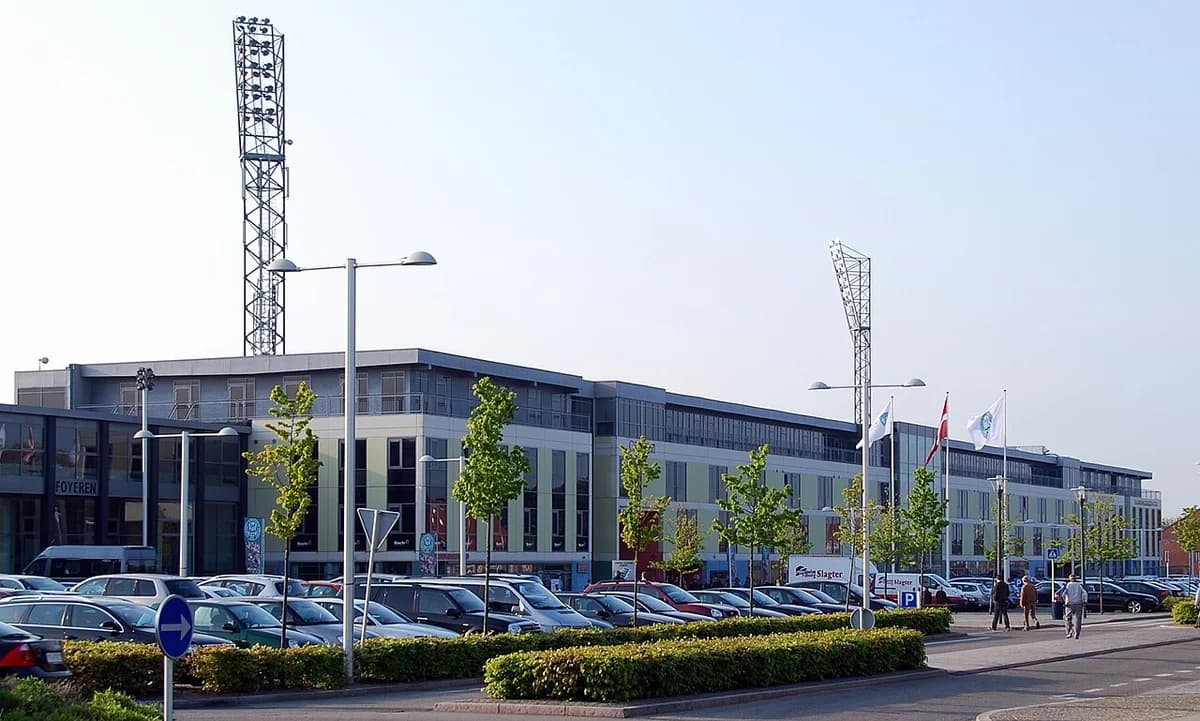 Exterior view of Viborg Stadium with light towers and a parking lot in front.