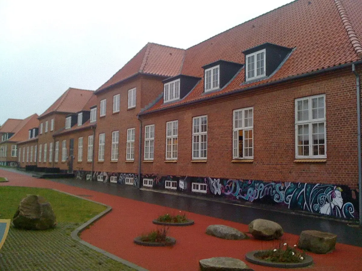 A brick building with a red tiled roof beside a courtyard with rocks and planted beds.