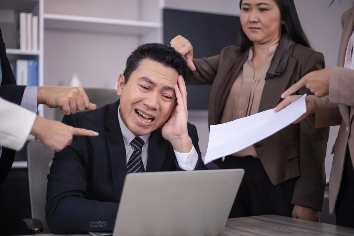 Stressed Asian businessman surrounded by colleagues in an office meeting