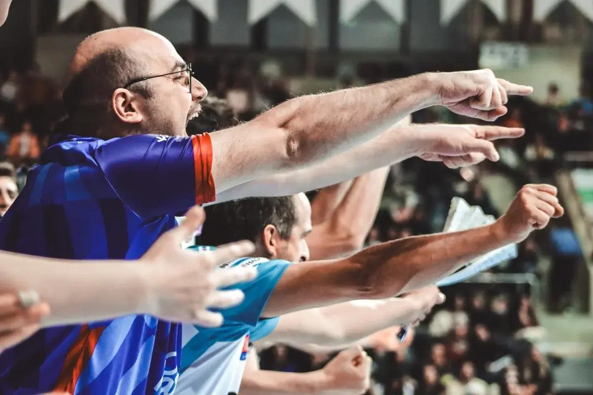 Sports fans in a stadium pointing and cheering during a match.