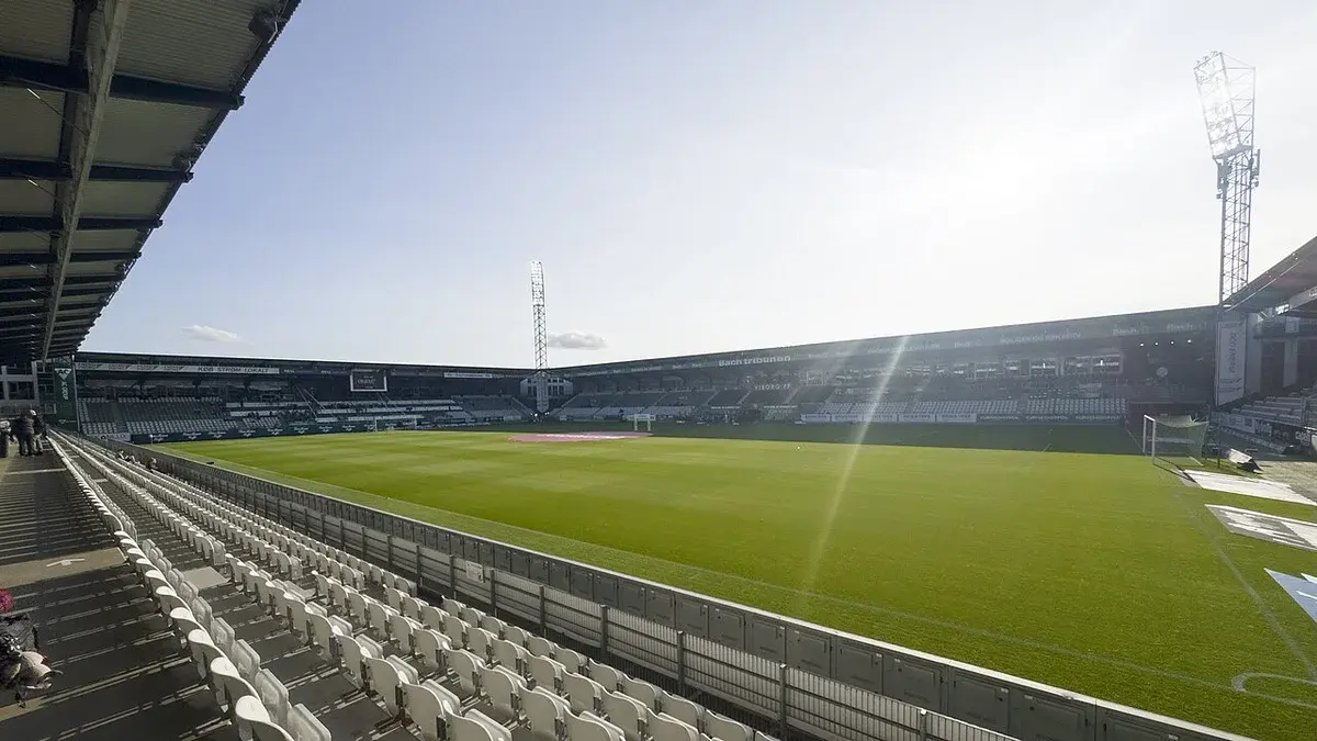 Wide interior view of an empty football stadium with green pitch and seating stands.