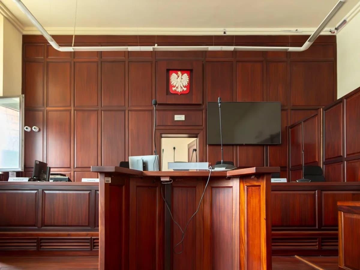 Wood-paneled courtroom interior with a Polish emblem above the judge's bench.