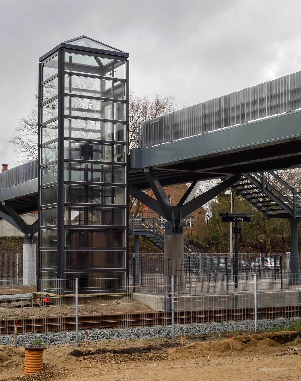 Glass elevator next to a pedestrian bridge at a train station.